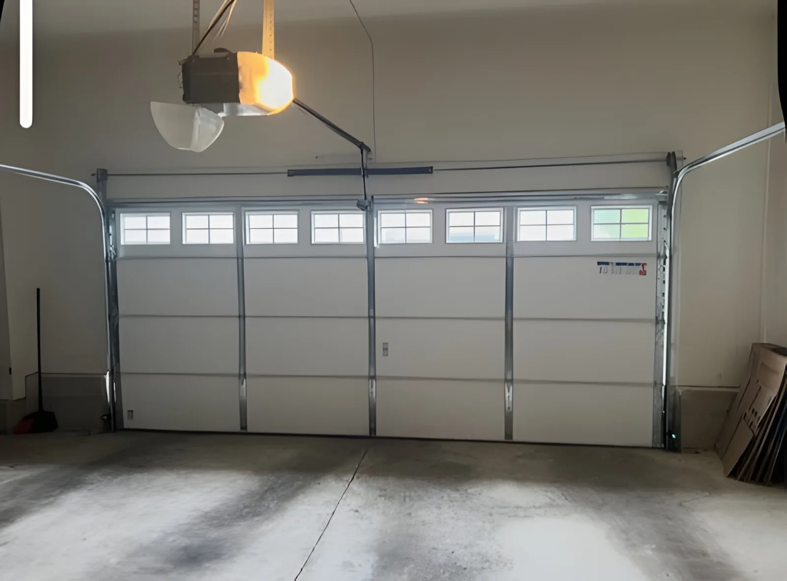 Interior view of a white sectional garage door with windows, tracks and automatic opener